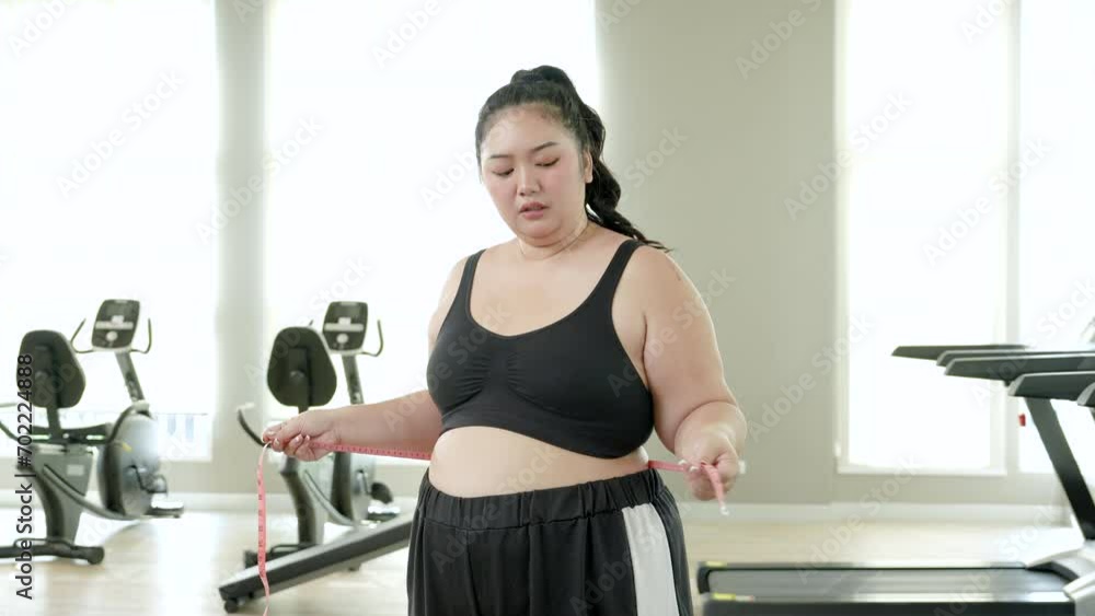 Asian chubby women hand using measurement tape measures her waist at gym, sad face for the result. Asian chubby women hand using measurement tape measures her waist at gym, sad face for the result.