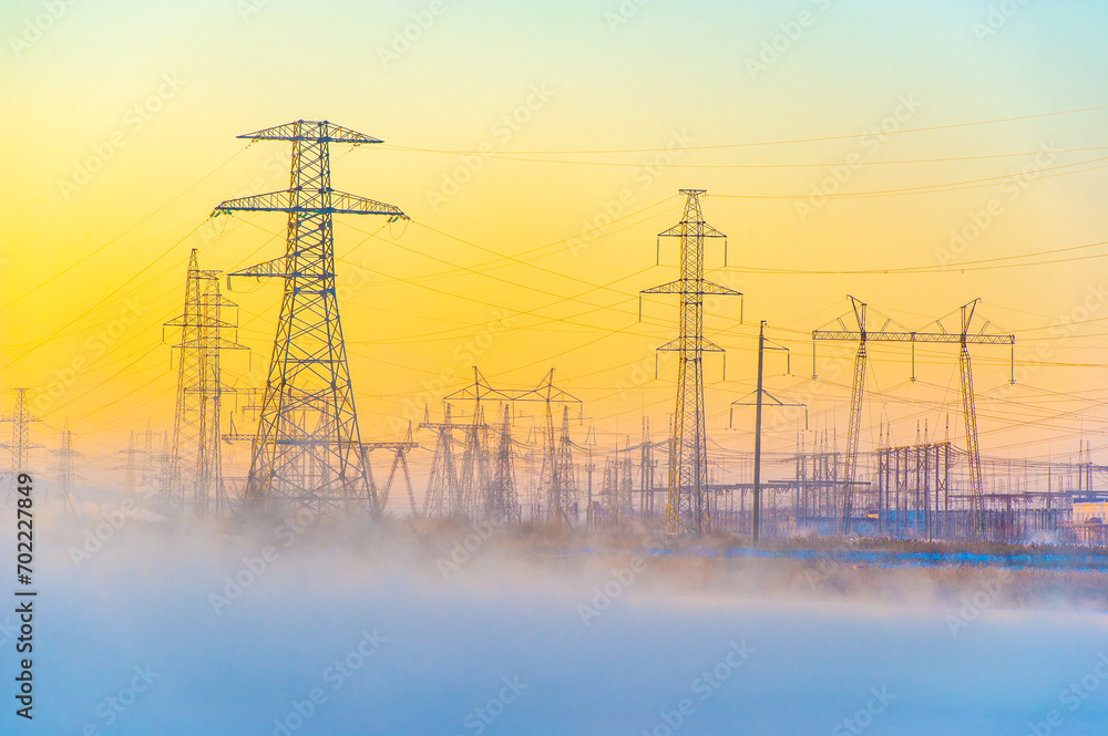 Powerful power lines stretching across a foggy river. Mysterious winter fog creates an unearthly atmosphere. The calm of the early morning is disturbed by the hum of electricity.