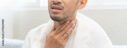 Sore throat in flu season. Young asian man touching her neck and feeling pain in throat in the bedroom at home. photo