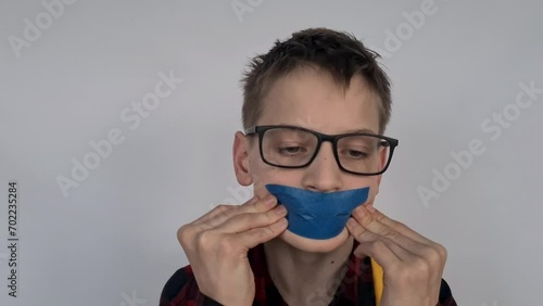 Portrait of a sad teenage boy with sticky tape on his mouth. Child rights concept and school bullying photo