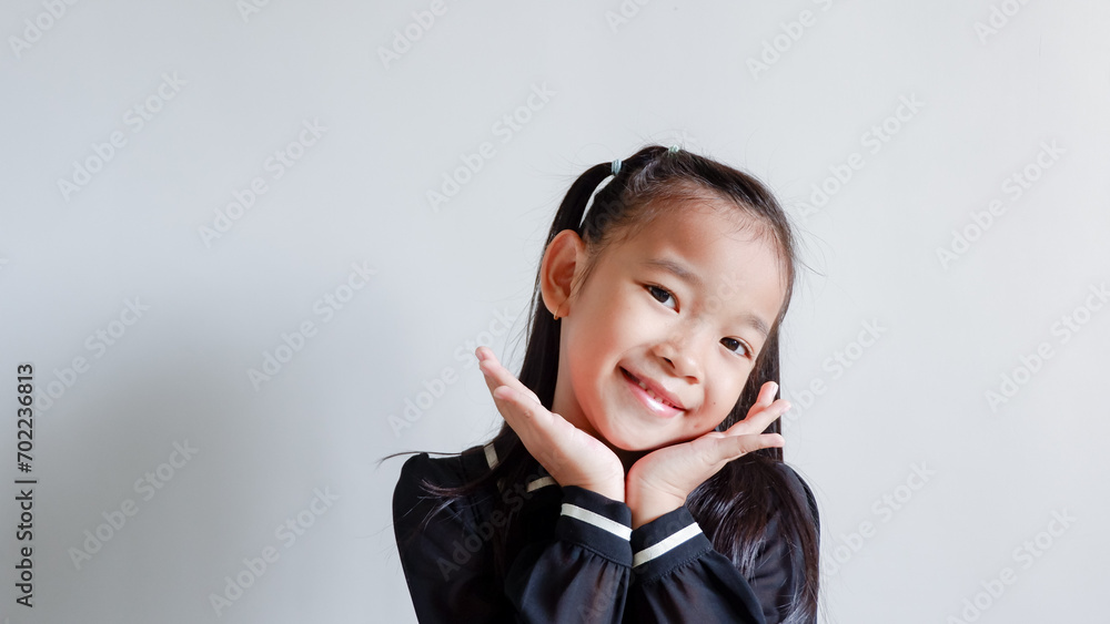 Closeup happy cute little Asian girl in black dress smiling over gray background Closeup happy cute little Asian girl in black dress smiling over gray background