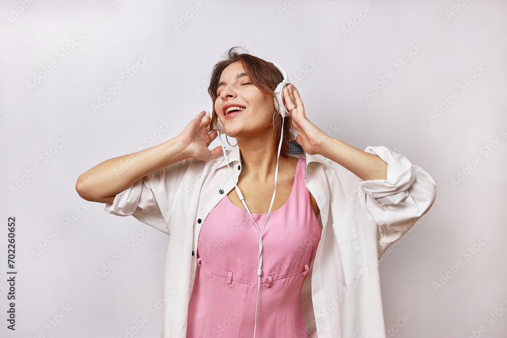Beautiful cheerful girl in a pink suit and white shirt listens to music in headphones. Beautiful cheerful girl in a pink suit and white shirt listens to music in headphones.