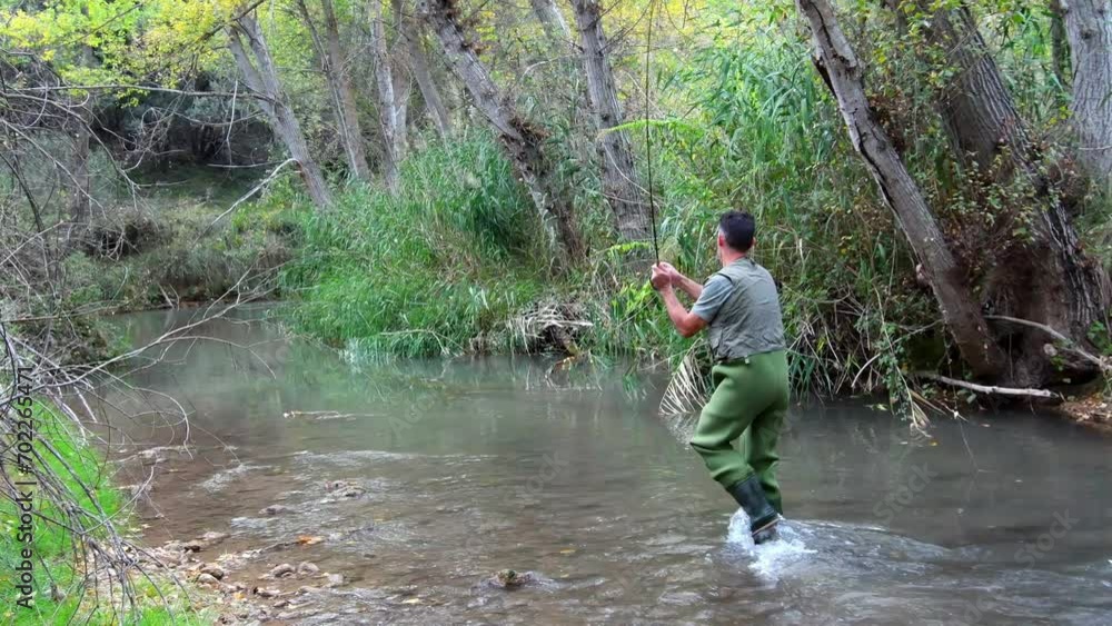 Fisherman in a vest and waders tucked into the river casting and retrieving his rattail fishing rod. Fisherman in a vest and waders tucked into the river casting and retrieving his rattail fishing rod.