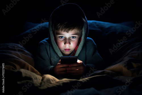 Boy looking at phone screen lying under blanket in bed in dark