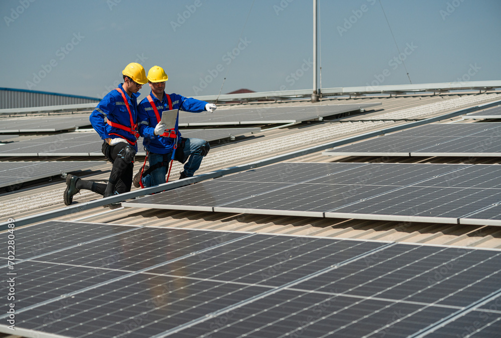 Men technicians carrying photovoltaic solar modules on the factory roof. Engineers in helmets installing solar panel systems outdoors. Concept of alternative and renewable energy. Men technicians carrying photovoltaic solar modules on the factory roof. Engineers in helmets installing solar panel systems outdoors. Concept of alternative and renewable energy.