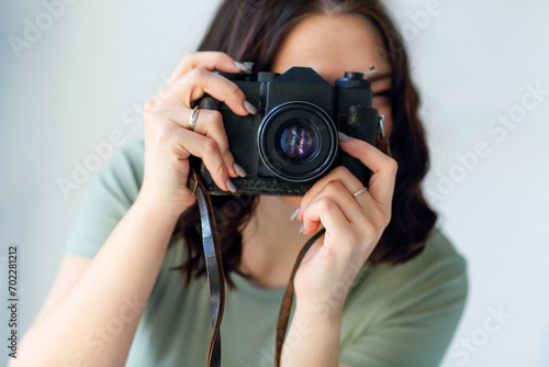 Young brunette woman photographer taking photo indoors, looking into lens during photoshoot
