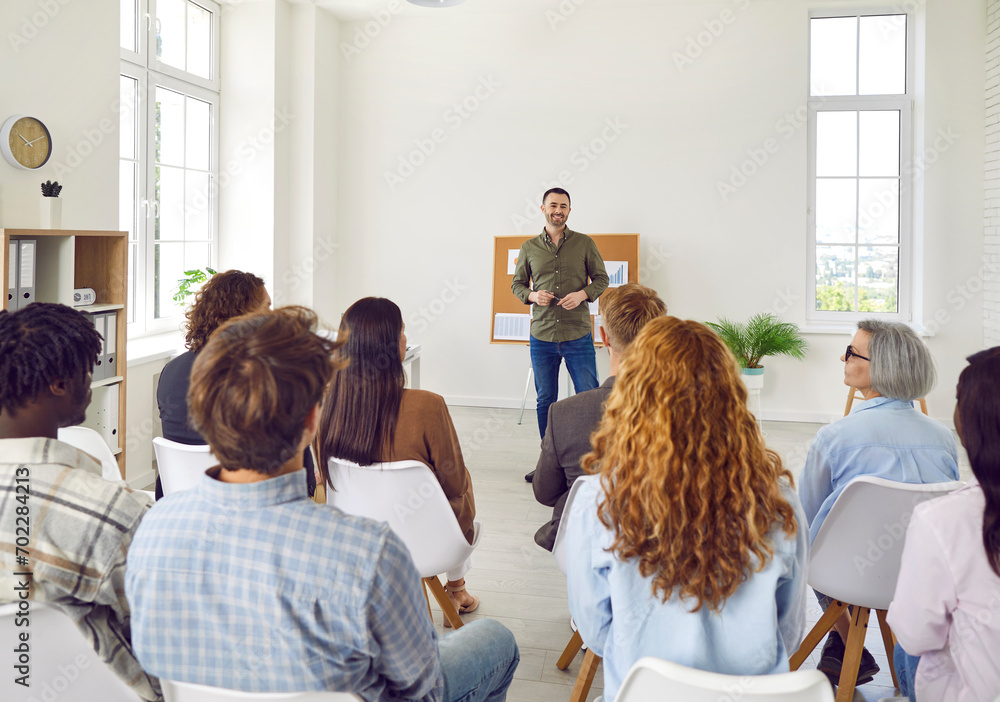 Employees attending corporate business training or seminar. Professional business coach speaking for multiethnic people in modern spacious office interior. Diverse audience, back view from behind - obrazy, fototapety, plakaty 