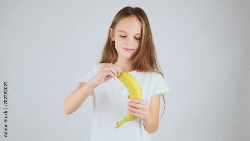 Cute child girl eating banana. Preteen girl peeling and eating banana, white background Cute child girl eating banana. Preteen girl peeling and eating banana, white background