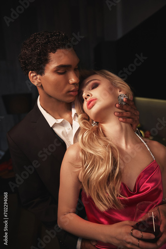 alluring sensual multicultural couple in evening attires with accessories hugging lovingly
