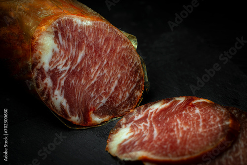 Close up view of cut of delicious Iberian lomo embuchado sausage cured in winery in Spain on black background with copy space photo