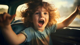 Happy young boy sitting in a driving or moving car, smiling and looking to the side. Joyful, cute and cheerful male child with curly hair enjoying his childhood, sun shining through the window