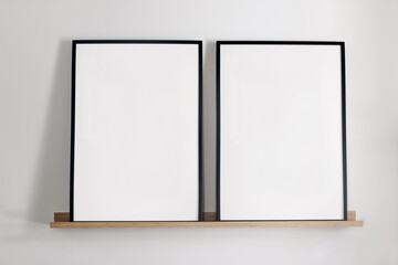 Artistic mockups template. Two black vertical picture frames on bamboo wooden shelf. White wall background. Posters at home, minimal Scandinavian design, no people. Elegant apartment concept.