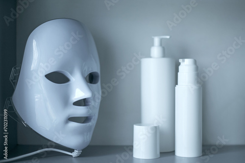 Light therapy LED mask on a shelf next to facial skin care products.