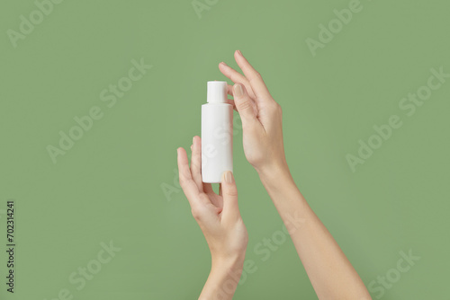 A womans hands holding a white cosmetic bottle on a green background