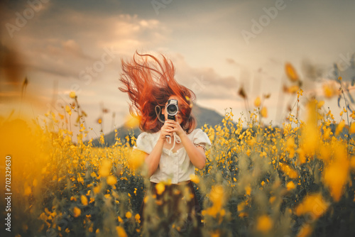 Young woman holds camera in yellow flower garden © Kanbokeh