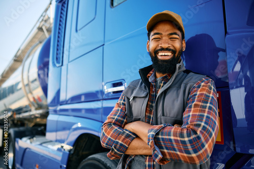 Cheerful black truck driver leaning on his vehicle and looking at camera. photo