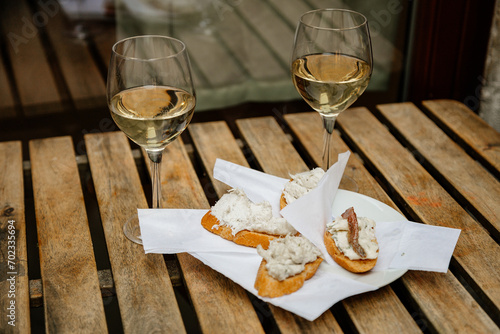 Venice, Italy, 12 February 2023:  Cichetti Venetian tapas with cod mash, cafe restaurant Bacari, Traditional Appetizers snacks accompanied with two glass of white wine, bar food, wooden table