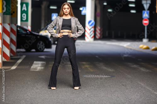 young girl with sunglasses in jacket posing near modern office building with mirrored walls in parking lot with road signs