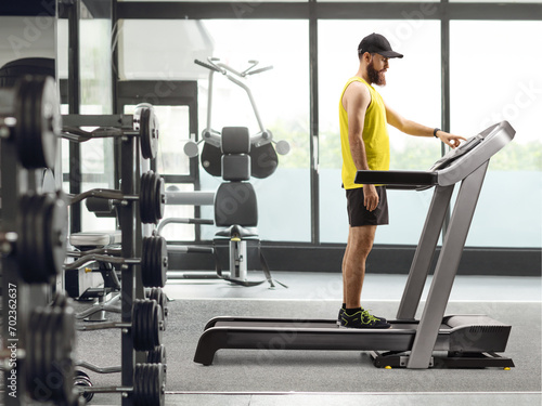 Full length shot of a bearded guy in sportswear standing on a treadmill and pressing a button