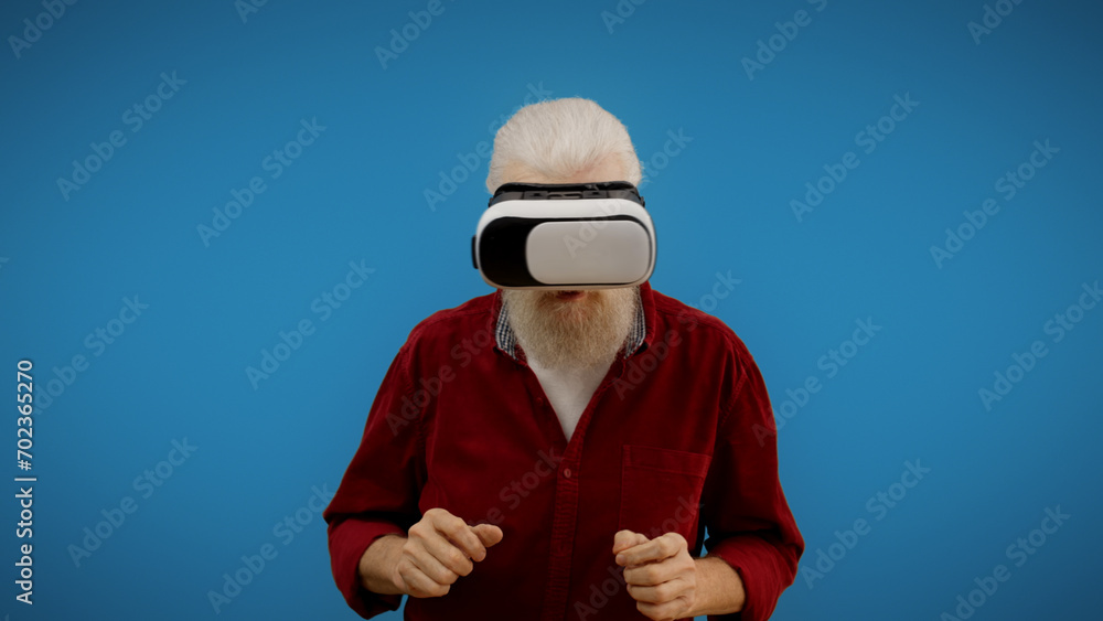 Senior man wearing VR glasses against a blue background, enjoying the wonders of futuristic technology Senior man wearing VR glasses against a blue background, enjoying the wonders of futuristic technology
