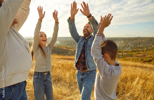 Portrait of happy joyful excited family standing in a circle in the field with two kids boy and girl with hands up enjoying nature during a walk together. Young parents with children walking outdoors