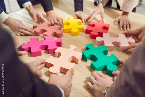 Business people put colorful puzzles on the desktop and present the concept of business cooperation, teamwork, support and assistance in the office. Hands close-up of office workers assembling puzzle.