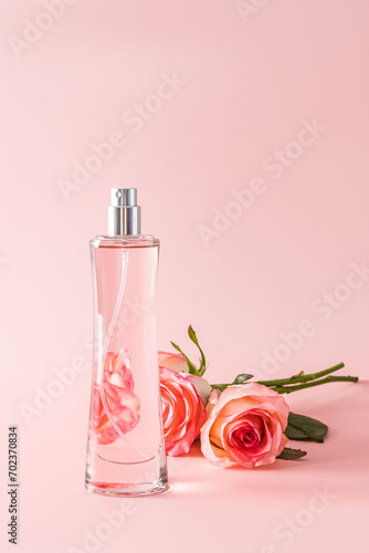 A chic tall bottle of women's perfume on a pastel background with a three tea rose. Vertical view. Presentation of the delicate fragrance of perfume.