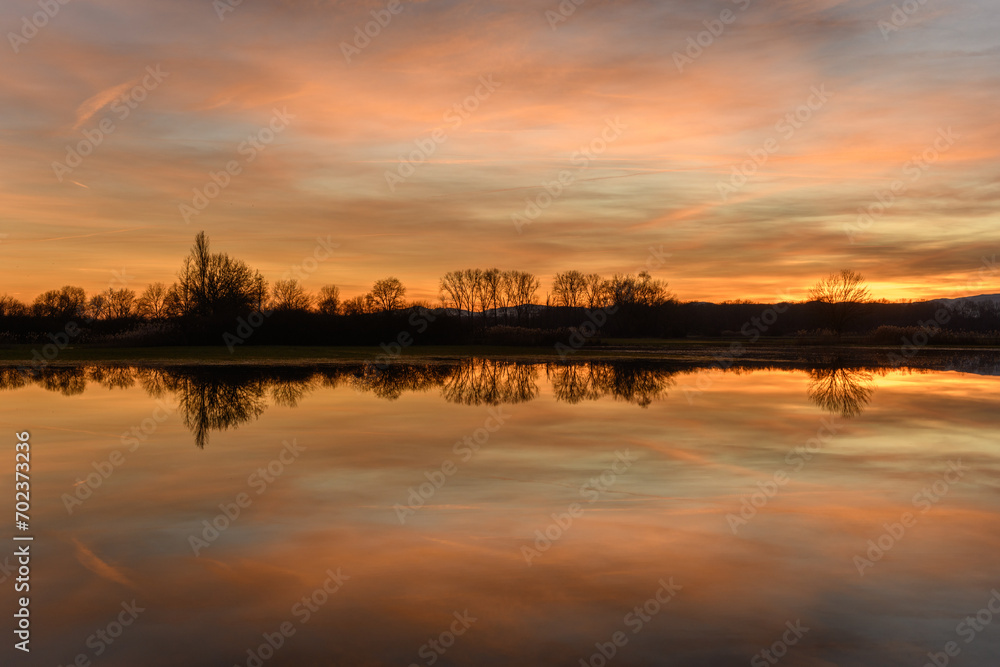 Trees reflecting in the water at sunset. Winter landscape red and orange sky.