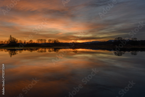 Trees reflecting in the water at sunset. Winter landscape red and orange sky.