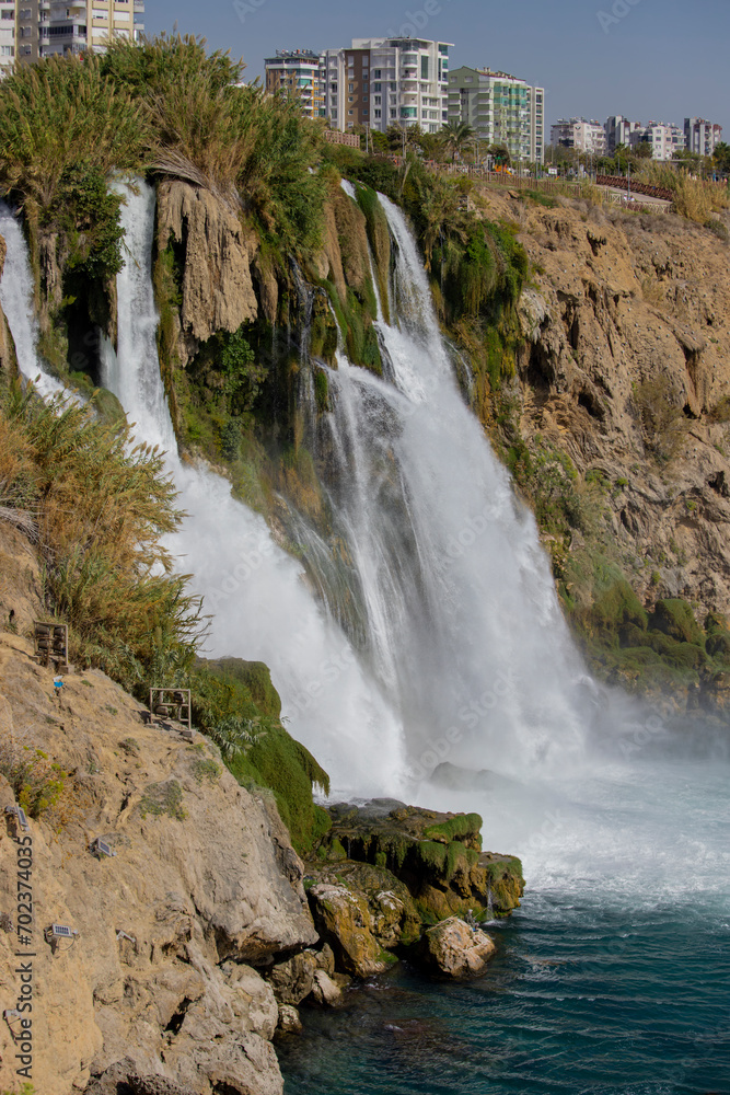 The moment when the Lower Düden waterfall flows into the sea, against the background of the steep shores of the Mediterranean and the urban development of the city of Antalya. The moment when the Lower Düden waterfall flows into the sea, against the background of the steep shores of the Mediterranean and the urban development of the city of Antalya.