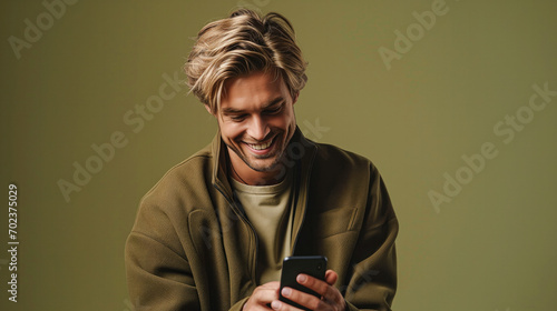 A handsome blond man is looking at a smartphone screen. Olive green monochrome studio background. © Roxy jr.