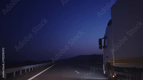White truck with cargo trailer driving on highway carrying goods at night, insured trucking. Free place on semitrailer for copy space, slow motion cinematic shot photo