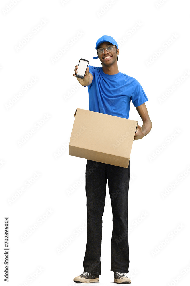 A male deliveryman, on a white background, full-length, with a box, shows a phone