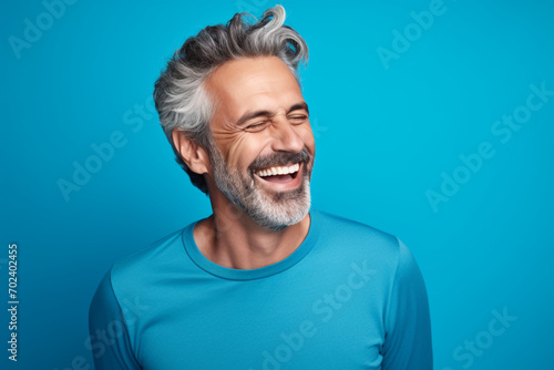 Middle aged man laughs against a blue background 