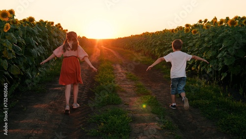 Brother, sister fantasize about flying into sunset. Cheerful children play, run with their hands raised in field of sunflowers in summer, dream of flying. Friends boy girl playing together in nature.