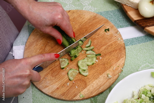 Hand cutting cucumber on wooden chopping board