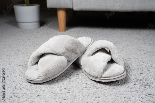 Modern grey slippers on the carpet near the sofa. Cozy and comfortable shoes for home