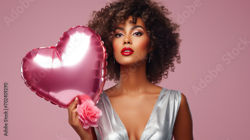 Woman with curly hair smiling while holding a heart-shaped balloon against a pink background. © MP Studio