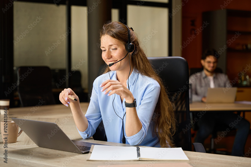 Female call center operator watching on laptop near her blurred male colleague Female call center operator watching on laptop near her blurred male colleague
