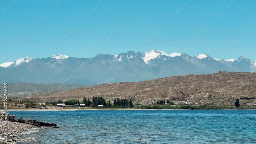 View of Issyk-Kul mountain lake, Kyrgyzstan. Waves splash on a sandy beach with rocks. Calm, peaceful natural background. Lake with a view of the Tien Shan Mountains. Kyrgyzstan 4K View of Issyk-Kul mountain lake, Kyrgyzstan. Waves splash on a sandy beach with rocks. Calm, peaceful natural background. Lake with a view of the Tien Shan Mountains. Kyrgyzstan 4K