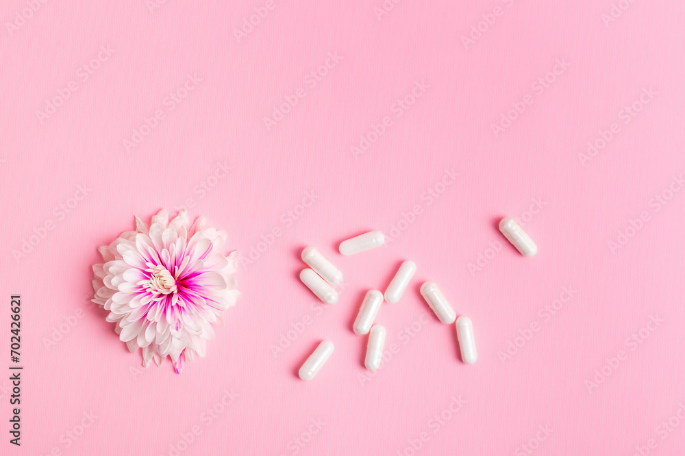 Horizontal photo of vitamin capsules and pink flower from above on a pink background. Healthy lifestyle. Food supplements and vitamins.