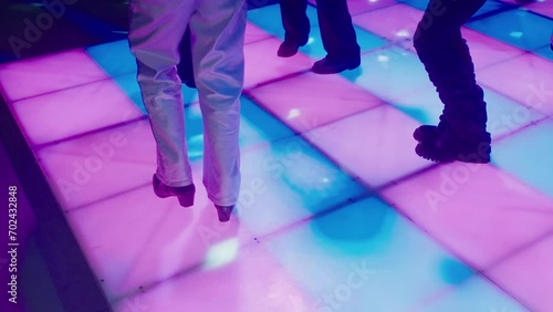 People in bell-bottomed trousers are dancing disco on disco floor glowing with multicolored squares. Vintage disco with dancing legs. Party at a nightclub in the style of 80s. Floor in a nightclub