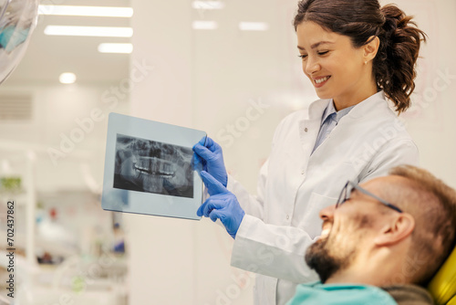 A happy dentist is showing jaw x-ray to a patient at dentist office.