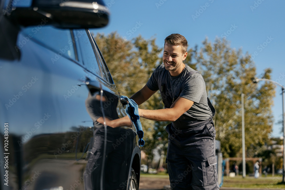 A happy car wash worker is using rug to polish a car.