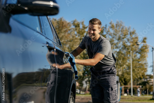A happy car wash worker is using rug to polish a car.