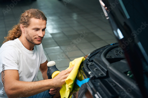 Mechanic in a car repair shop polishes headlights of car