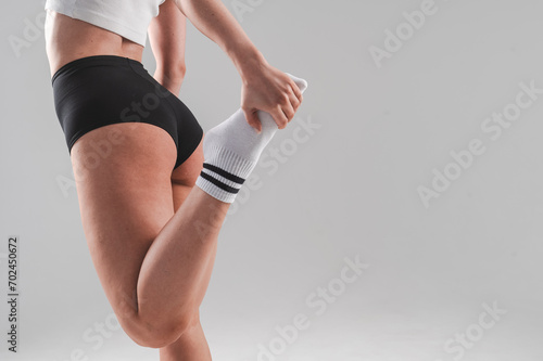 Fotografi Faceless woman stretching her quadriceps on a white background.