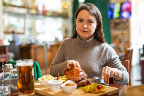 Female traveler tasting fried pork ham knuckle traditionally served with stewed cabbage  pickled vegetables  various sauces and beer in cafe in Vienna. Popular snacks