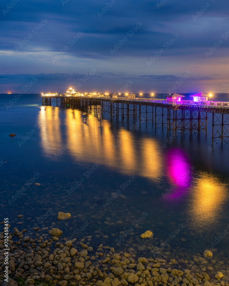 Fototapeta premium Long historic pleasure pier at dusk with lights reflecting in the water. Llandudno seaside resort, North Wales