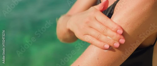 Close up of young woman applying a sunscreen or sun tanning lotion on a shoulder to take care of her skin on a seaside beach on vacation.